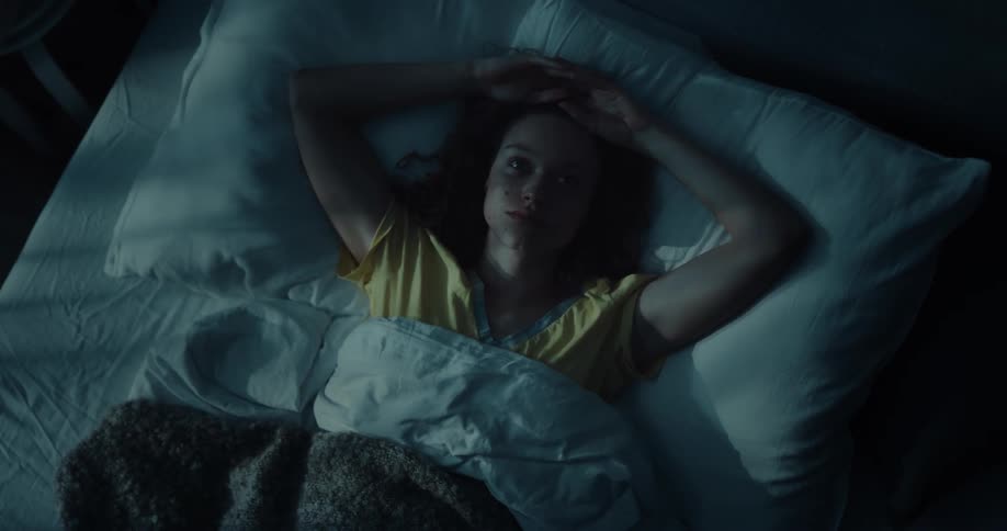 A woman lying in bed on her back fidgeting unable to sleep