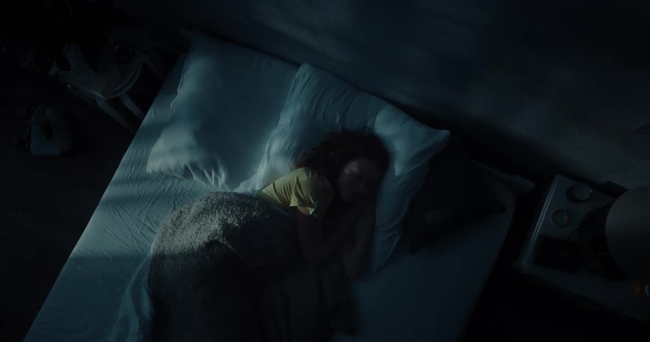 A woman lies down in bed in a dark bedroom