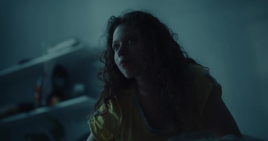 A woman is sitting in a dark room and takes a pill with some water