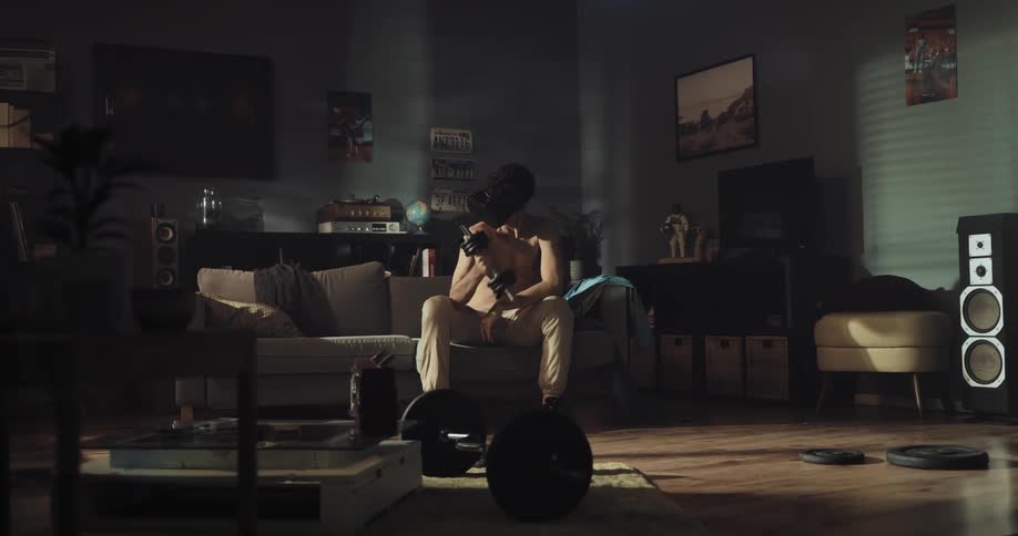 A young man wearing a virtual reality headset lights a small weight while sitting on the couch