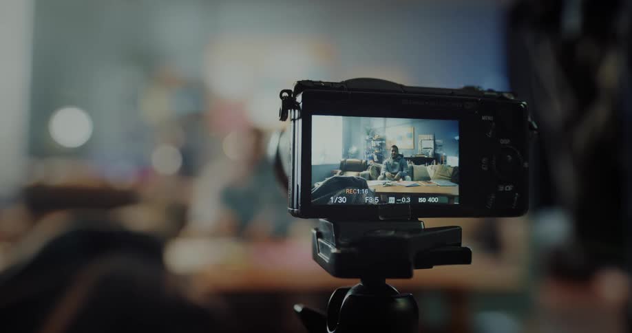 A man has a camera set up to take a photograph then sits on his couch in front of it