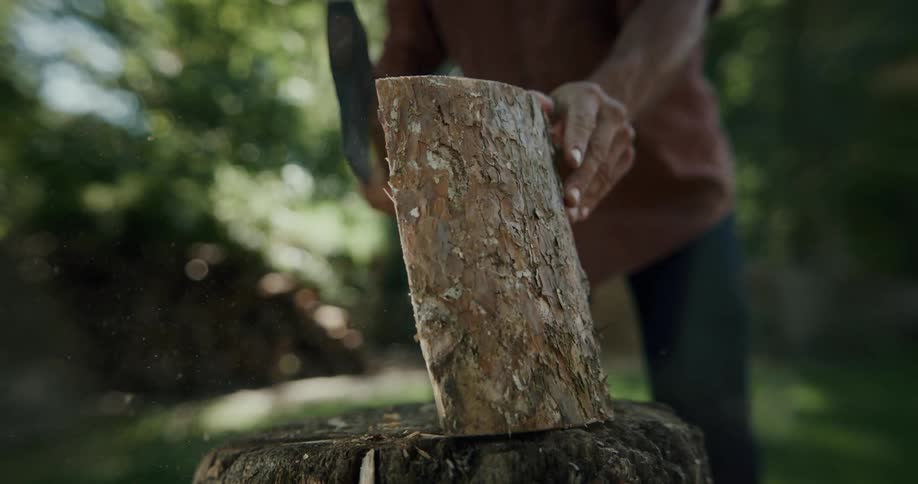 Close up of a man chopping a piece of wood with an ax over a stump outodoors