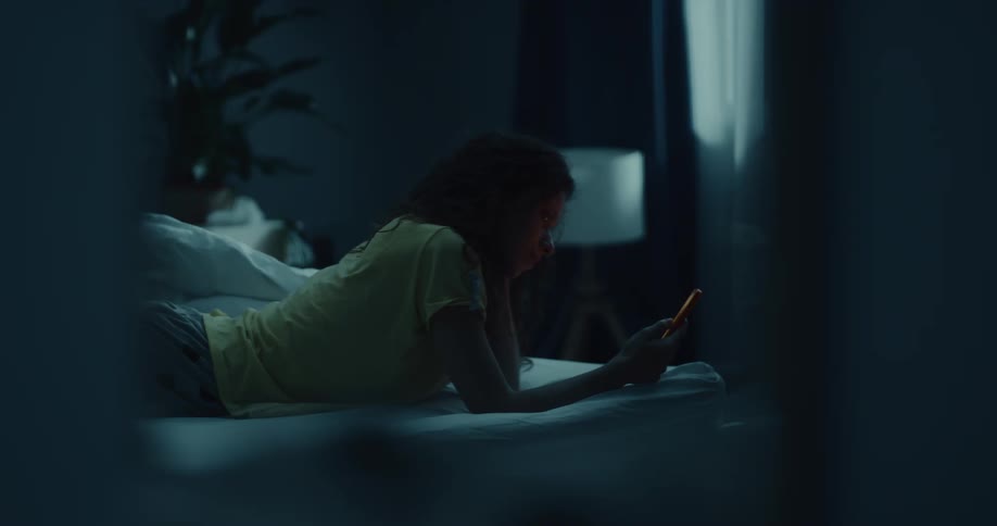 A young woman plops down on her bed and scrolls through her phone
