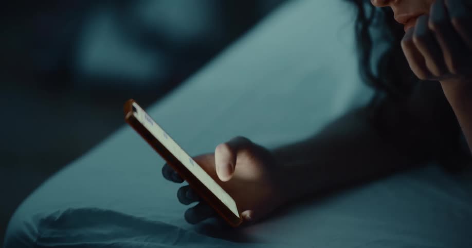 A woman lying in bed with head resting on her hand scrolling on her phone
