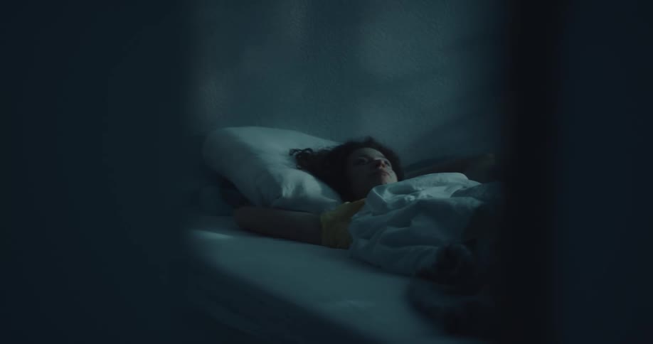 A woman restlessly turns over in bed with the shadow of trees on the wall above her
