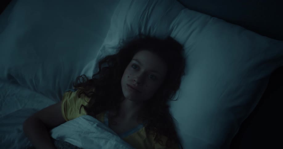 A woman lies in bed and stares up at the ceiling