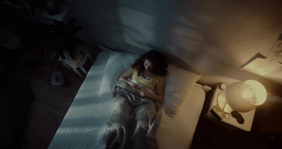 Woman reclines on bed scrolling through her cellphone