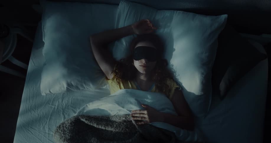 A woman lying in bed on her back wearing a sleep mask trying to sleep