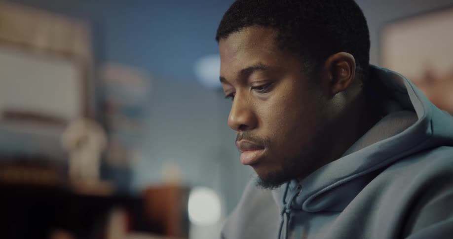 Close up of the face of a young man sitting in his bedroom looking down