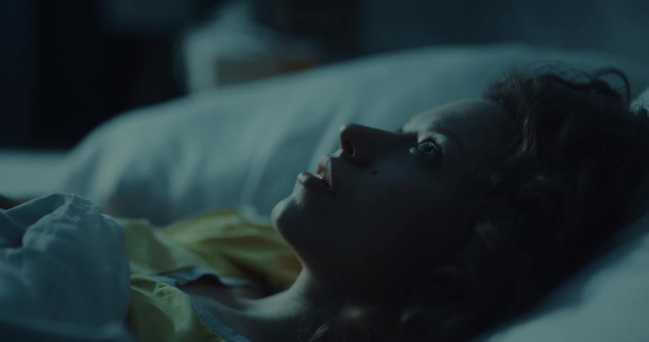 A woman is lying awake in bed at night and briefly puts her hand over her mouth