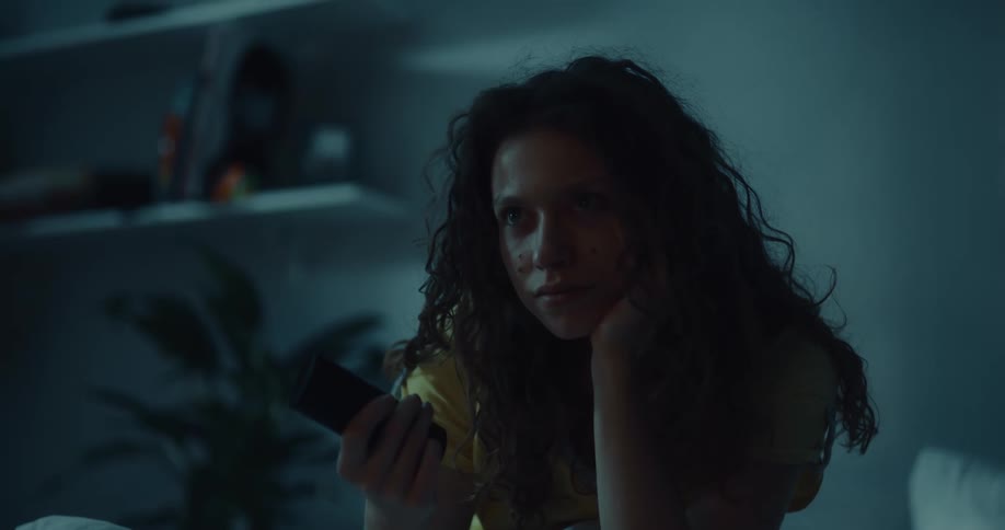 A woman sits up in bed grabs the remote and turns on the tv since she cant sleep