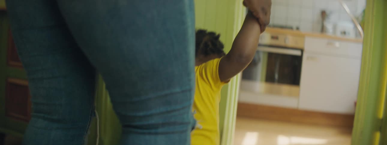 Mother with ripped jeans walks toddler girl wearing yellow clothes in the living room