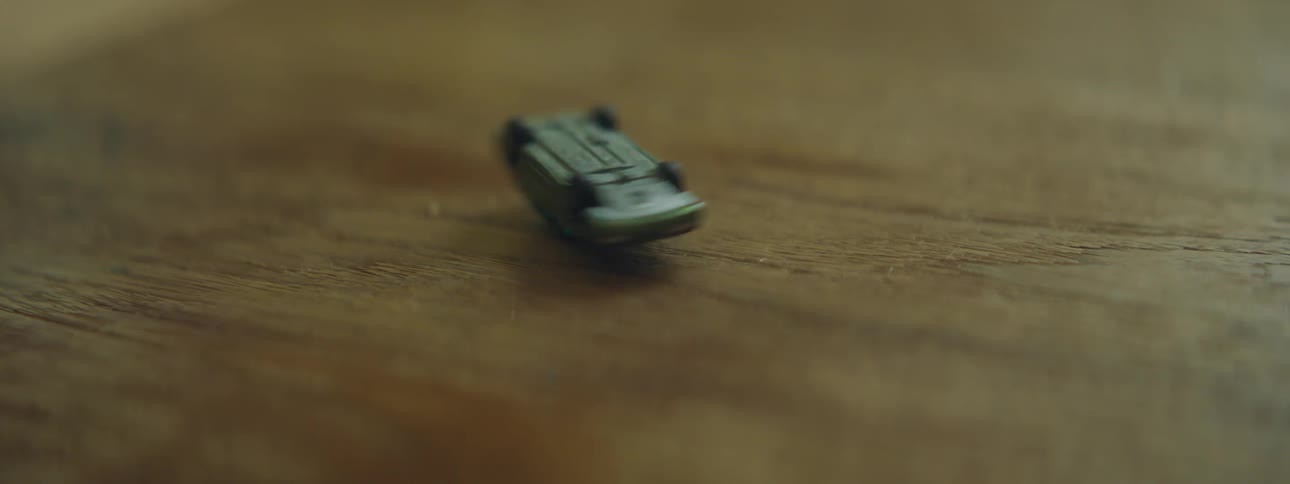 A black child spins a toy car on a wooden table