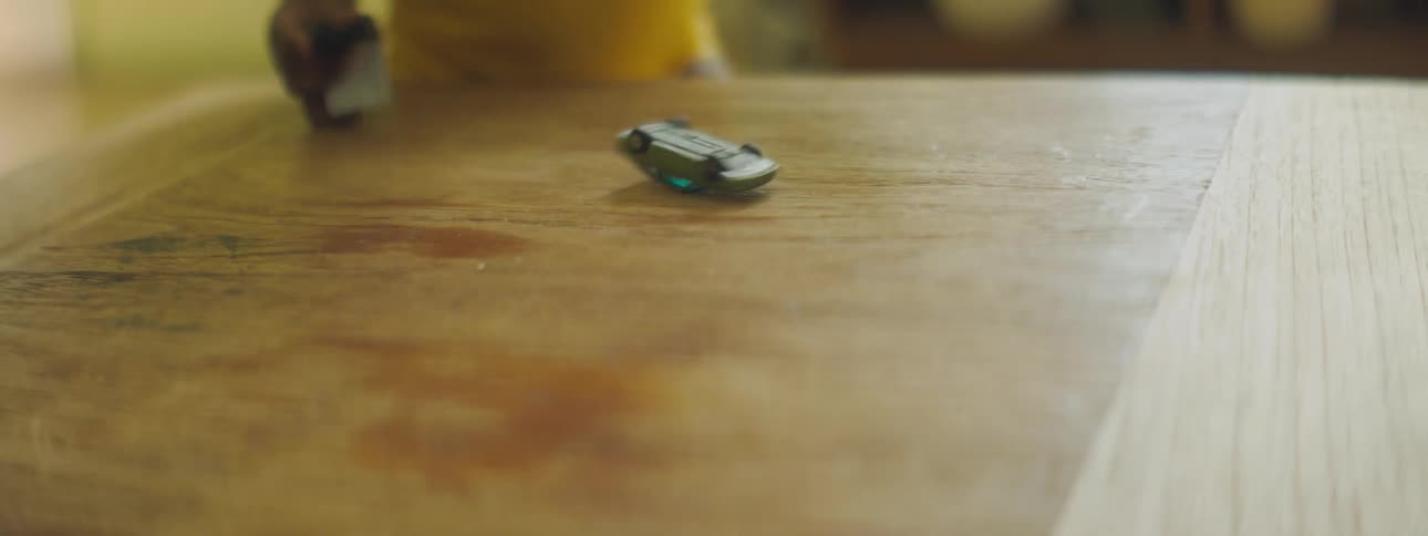 Person spins toy car on wood table then toddler walks over to pick car up