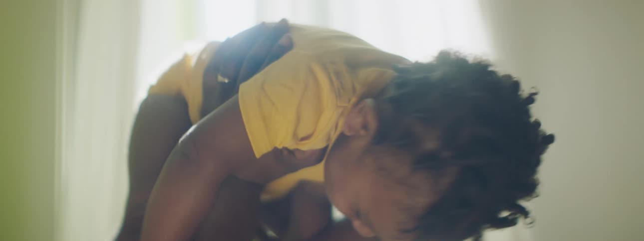 Woman lies on floor playfully holding child in air