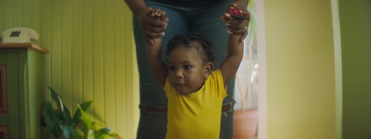 Mother with ripped jeans walks toddler girl wearing yellow clothes in the living room