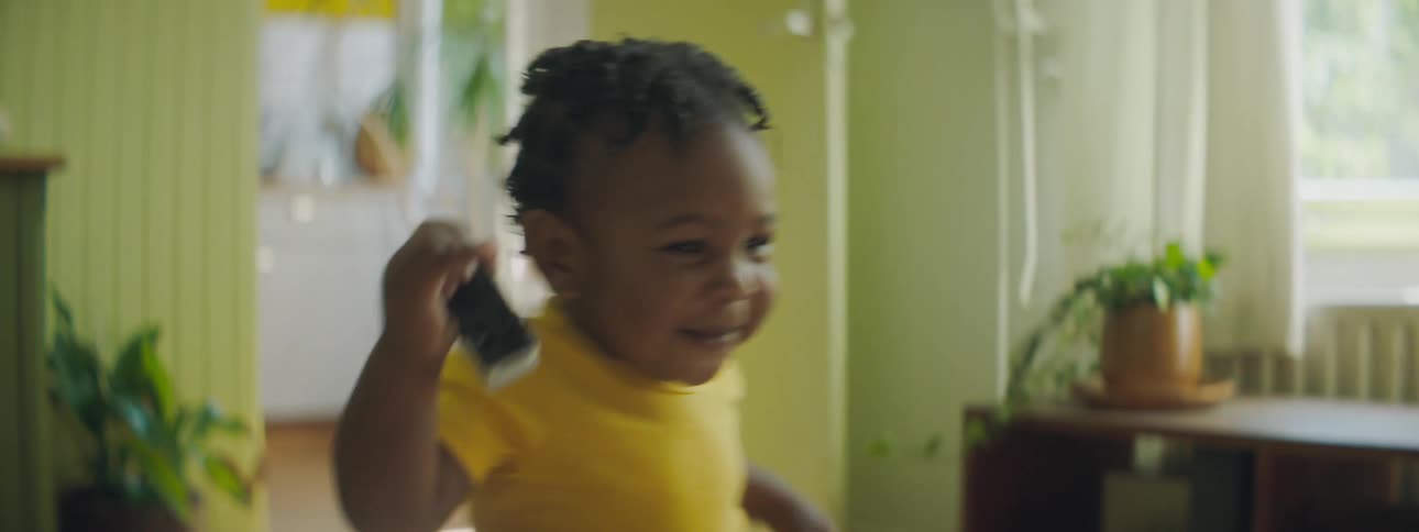 A baby stumbles walking across the room holding a toy car