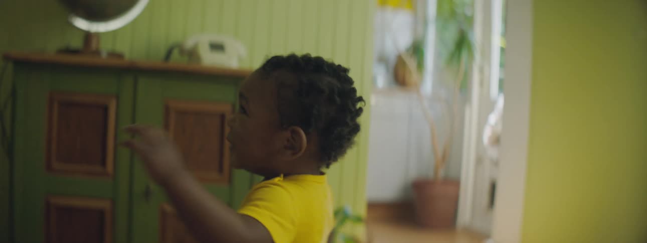 Black toddler girl with yellow clothes wanders around in the living room at home