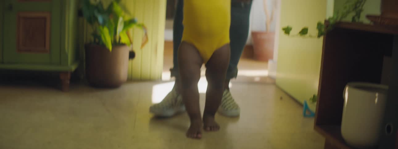 Mother with ripped jeans and shoes helps toddler girl walk in the living room at home
