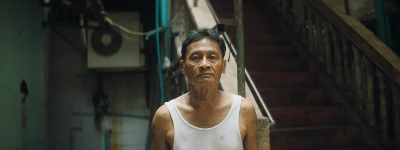An elderly asian man stands in front of a staircase