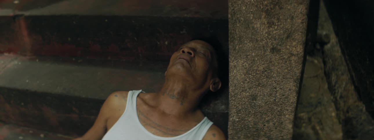 The corpse of a man with a bullet wound in his abdomen lying at the bottom of a cement staircase outdoors during the day