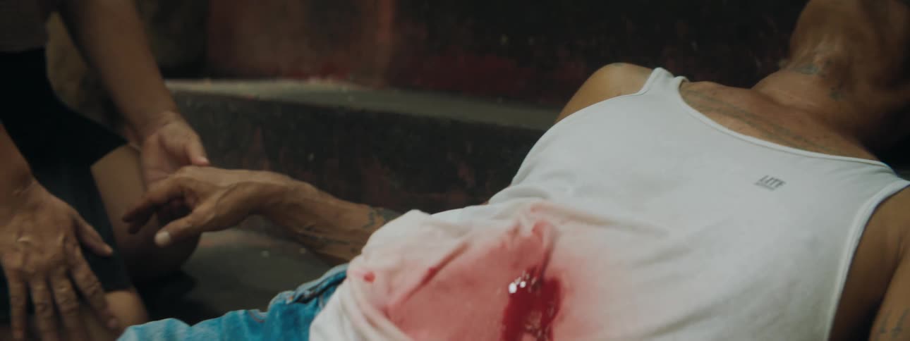 A woman holds a mans hand as he lies in the street bleeding