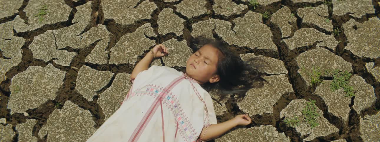 Child lies on back with eyes closed on cracked arid earth