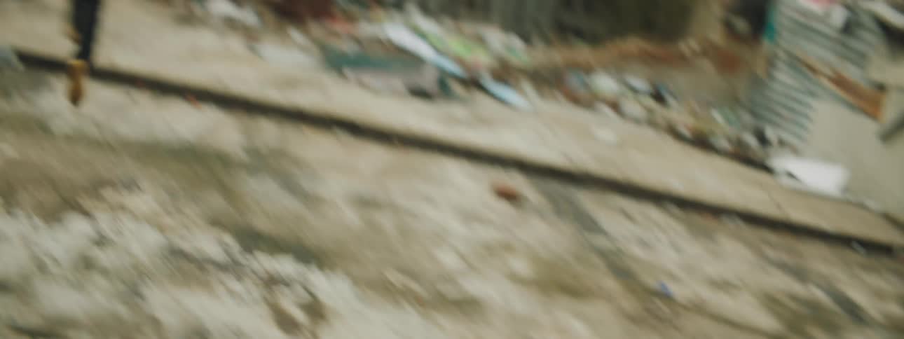A young boy squirts a girl with a water gun as they run around an outside rundown urban lot