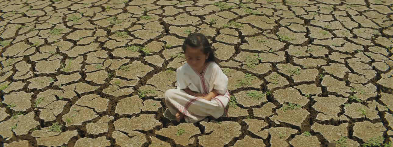 Girl sits on cracked arid ground cross legged with eyes closed