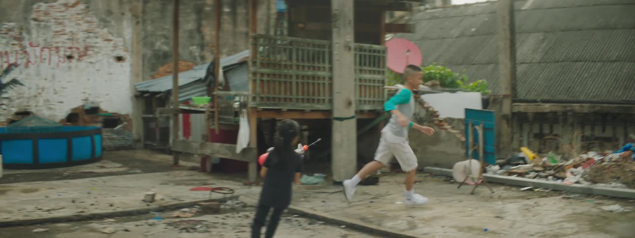 A girl chasing a boy with a water gun with buildings the sky and clouds in the background
