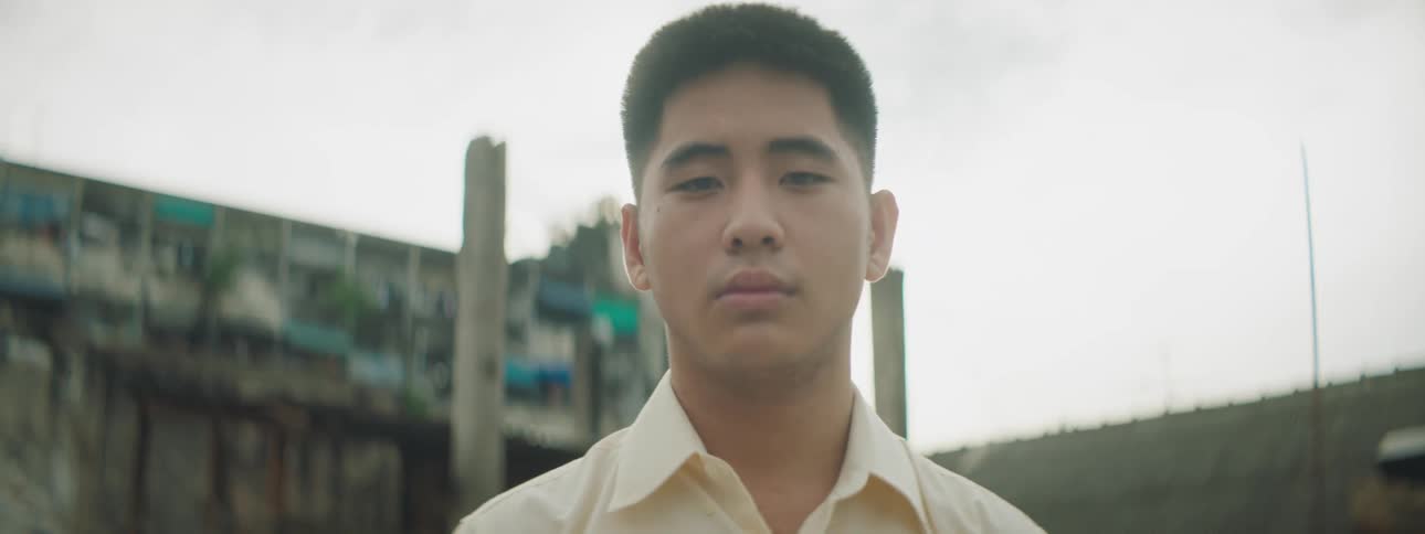 A young asian man standing in front of a building in a neighborhood