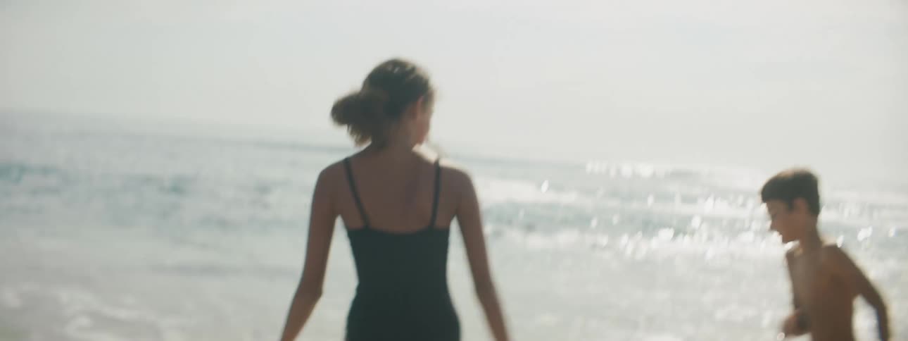 A boy and girl in swimsuits walking in ocean waves on a sunny summer day