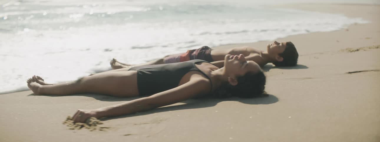 A brother and sister lie on the beach as the water rolls up the shore and over their bodies
