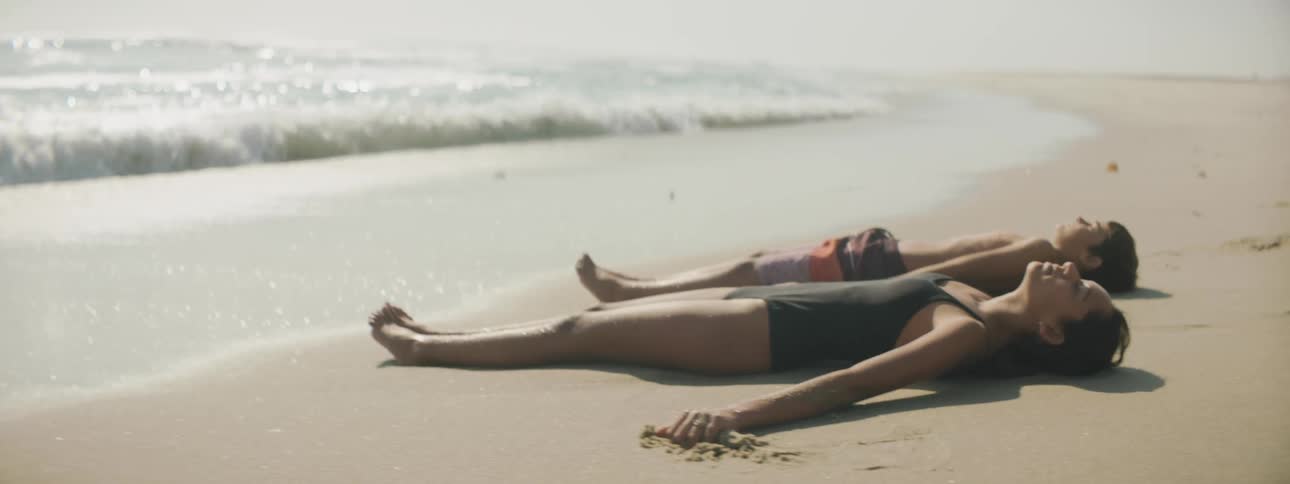 A boy and girl lie on the beach as water rolls towards their feet