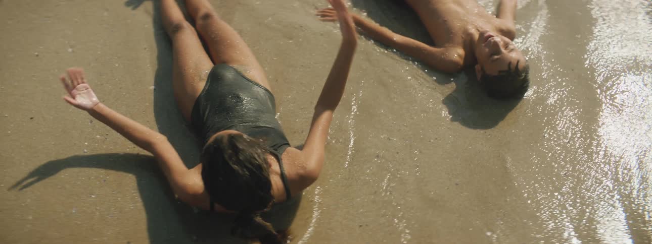 Boy and girl are pushed by the waves while laying on their backs on the beach