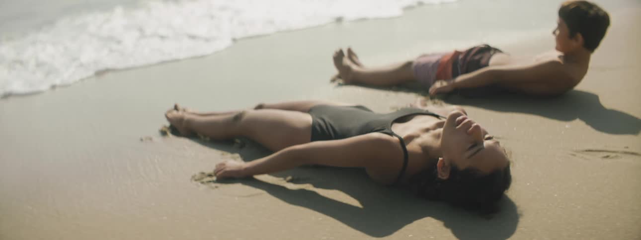 A boy and girl quickly lay on their backs in the sand just before the ocean wide washes around them