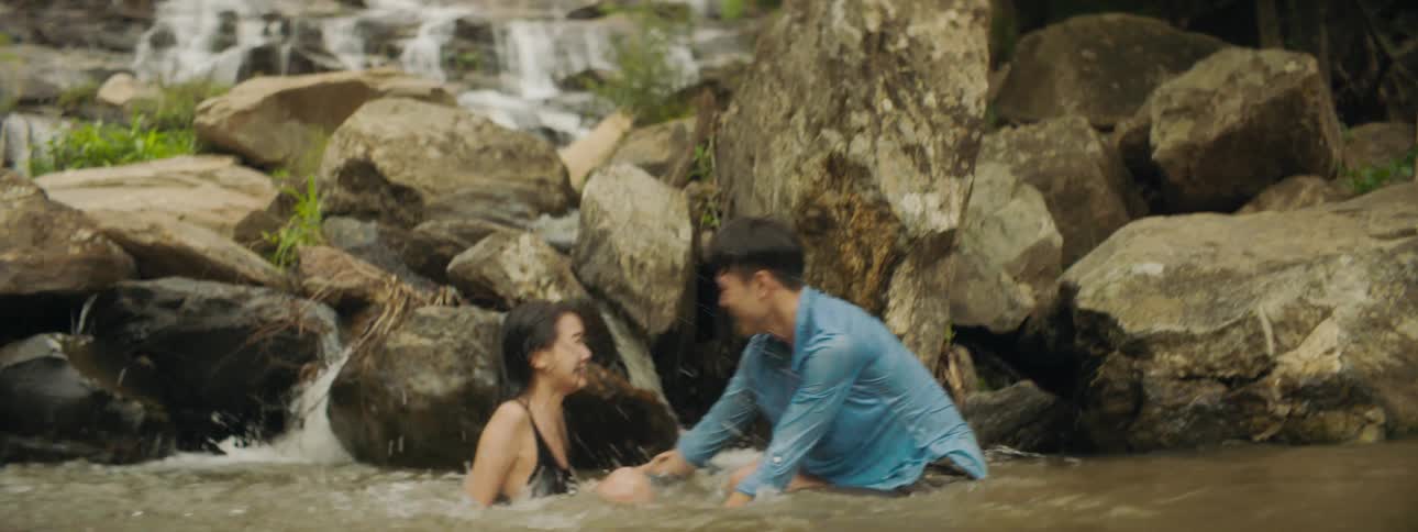 A man and a woman playing in a river splashing water at each other