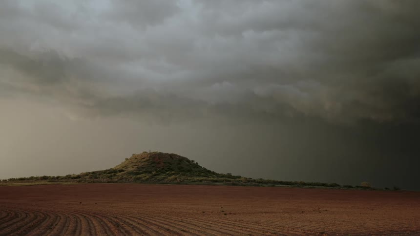 Dark storm clouds and lightning move over a mountain near rural farmland