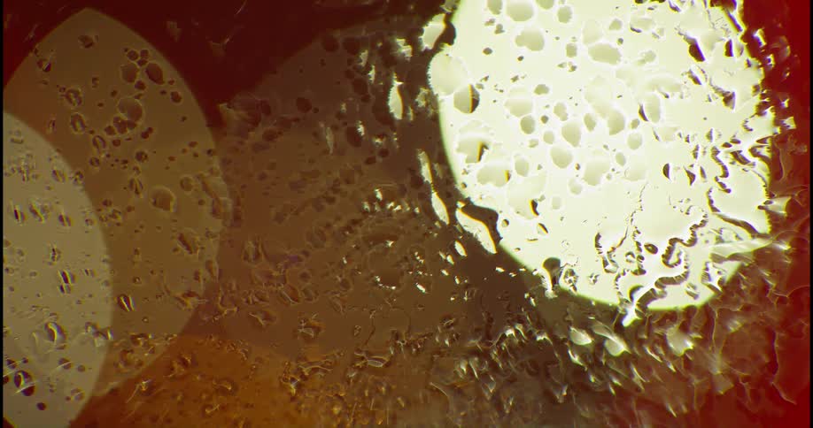 Rain falls on a window and there are bokeh circles of light behind it