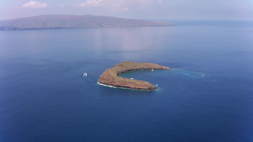 Boats are sailing around molokini island as waves move in the deep blue water