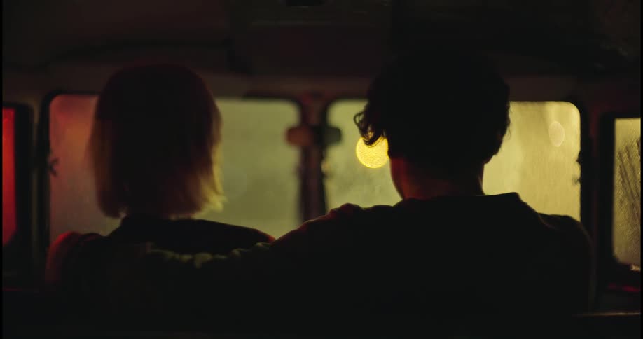 A man puts his arm around a woman and she scoots closer as they both look out a car window