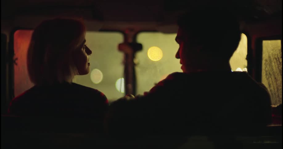 A young man and woman sit in a car, talking during a rainy night