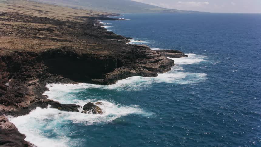 A jagged ocean coastline at the bottom of a hill during the day