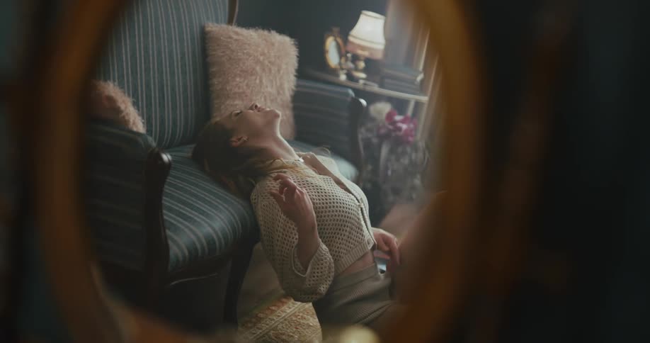 An oval mirror on a wall reflects a woman sitting on the floor dancing and playing air guitar