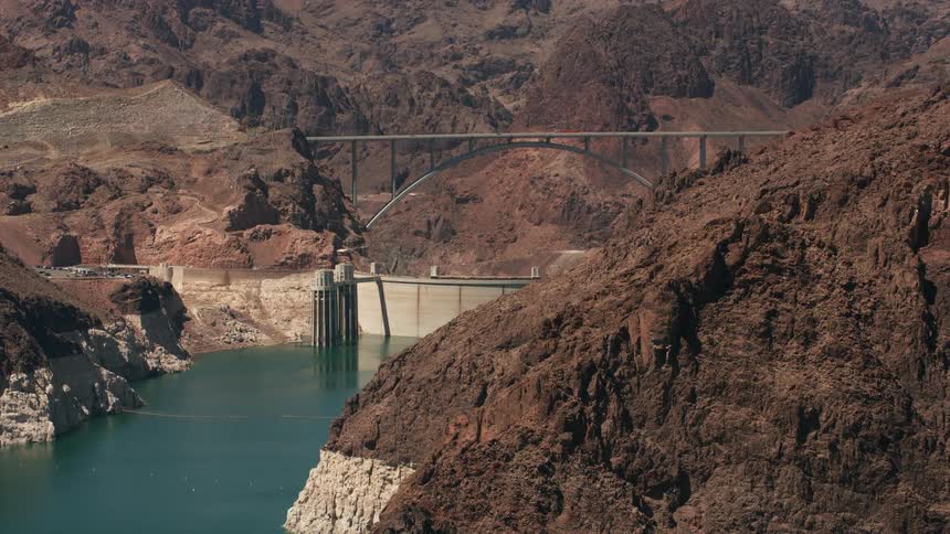 Traffic moves across a bridge over a mountain river canyon and there are boats in the water