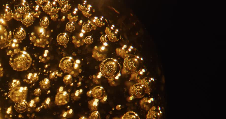 Small golden bubbles float in larger translucent amber sphere that gleams as it rotates in the darkness