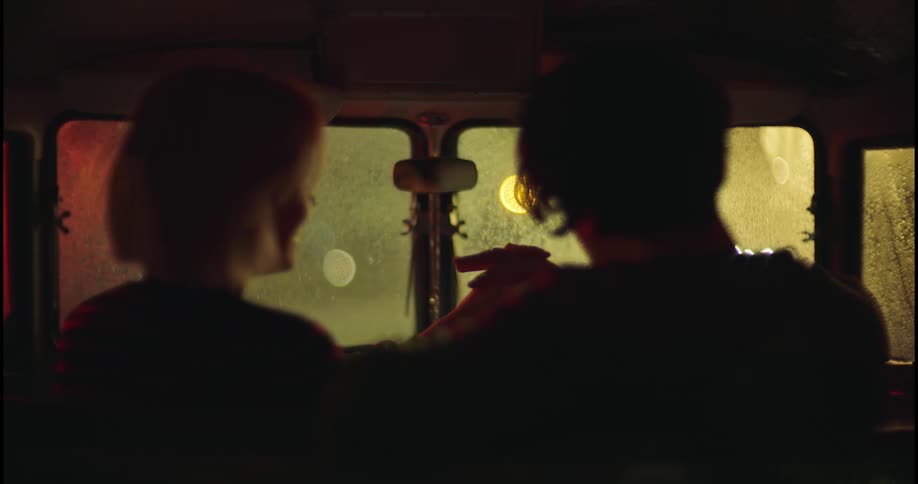 A couple sits together in a car and hold hands on a rainy night