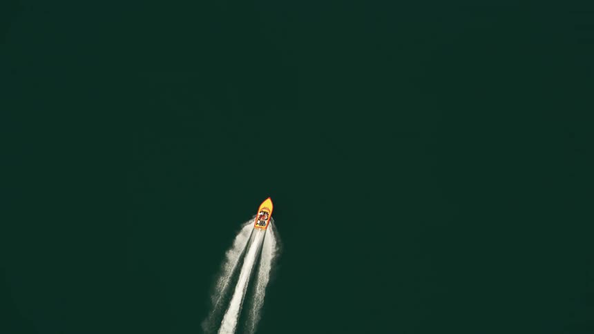 A yellow motorboat leaves a white wake as it travels through smooth water