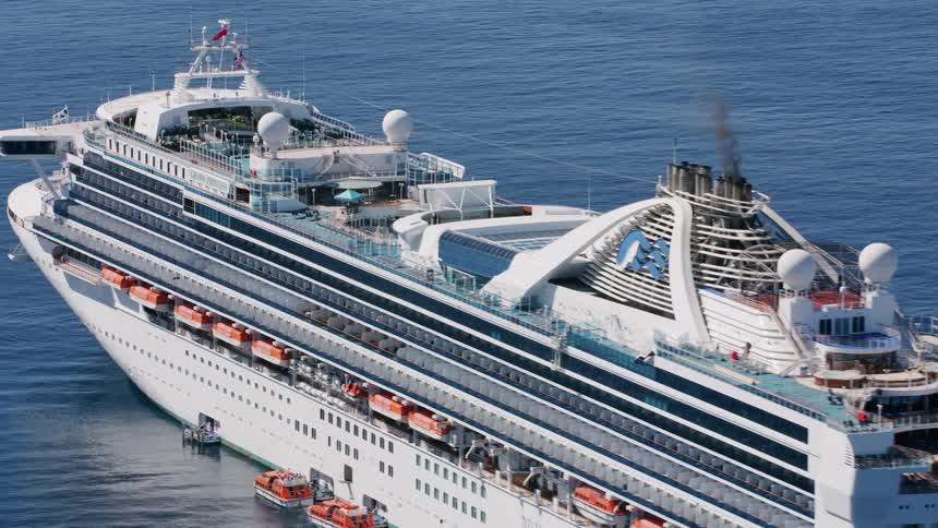 Cruise ship moves across water with lifeboats and other boats attached