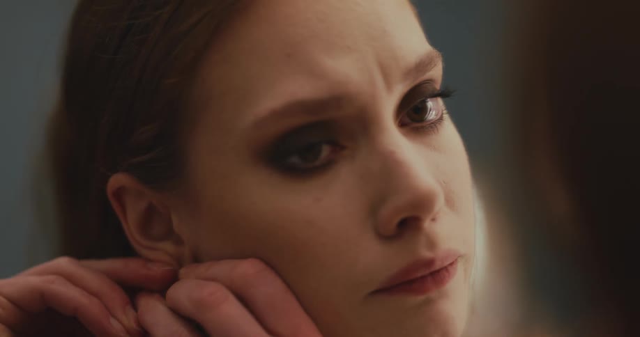 Teary eyed woman removes her earring while looking at herself in the mirror